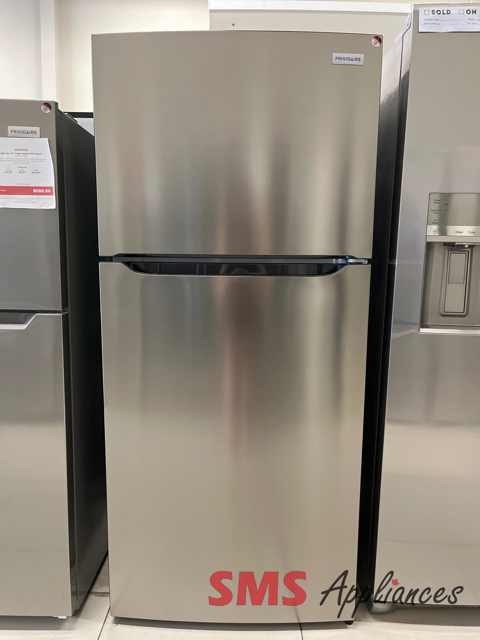 Open-Box-Fridges-FRTE1835AV-2-3-scaled-1.jpg Stainless steel Frigidaire refrigerator on display in a showroom, with a bottom freezer drawer and a partial SMS Appliances logo visible at the bottom edge.