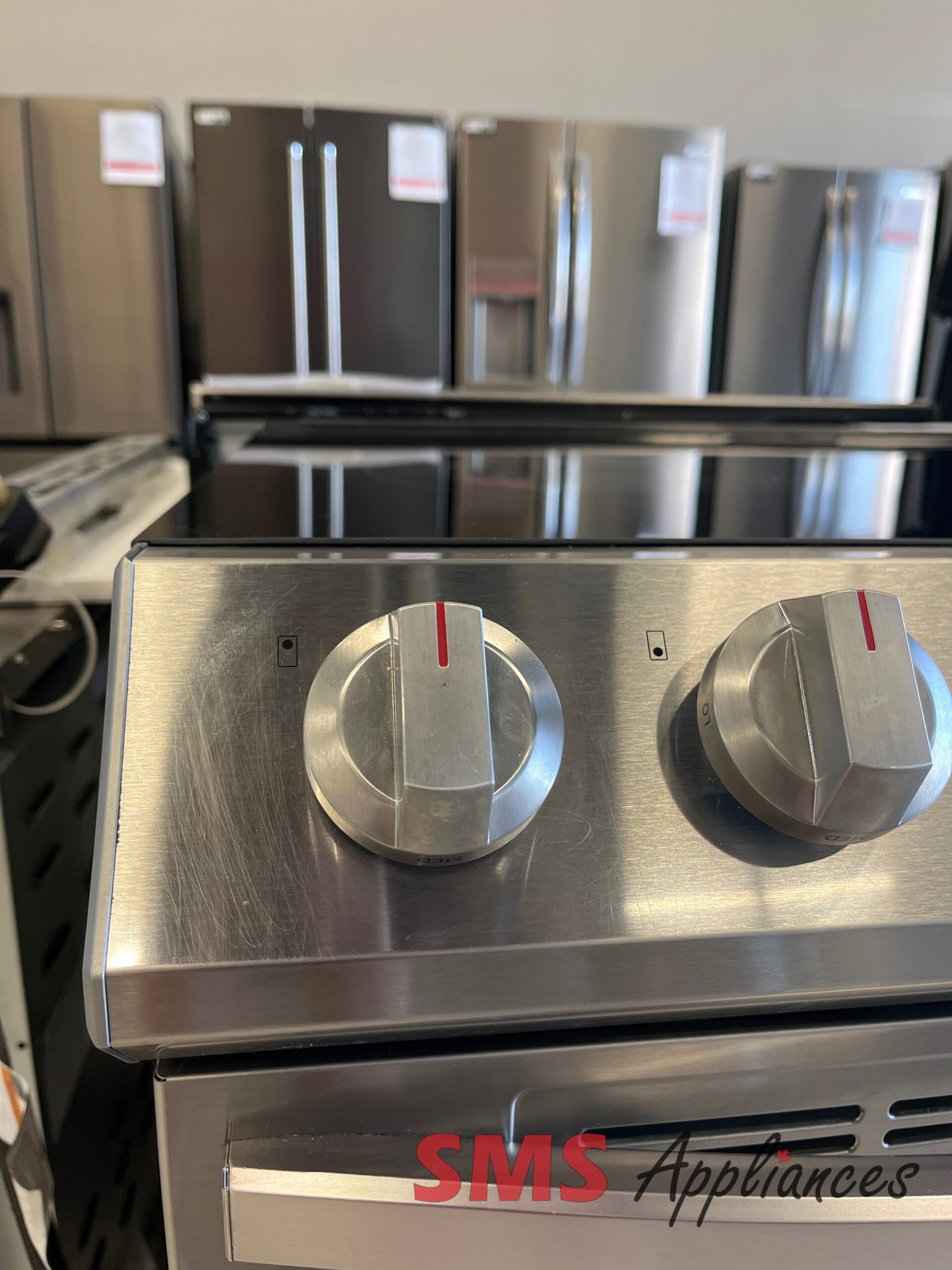 Refurbished-Stoves-Ranges-NE63T8111SS-5-scaled-1.jpg Stainless steel range with two large control knobs on a brushed metal surface; 'SMS Appliances' logo visible below.