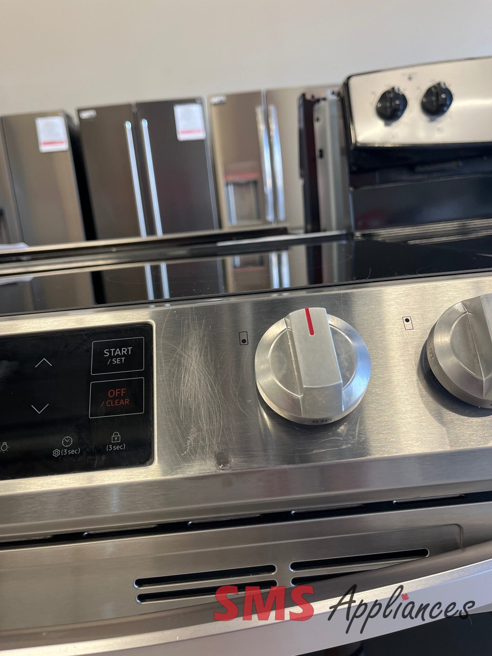 Refurbished-Stoves-Ranges-NE63T8111SS-8-scaled-1.jpg Close-up of a stainless steel oven/range with large metal knobs and a digital control panel (Start/Set) on the left side area.